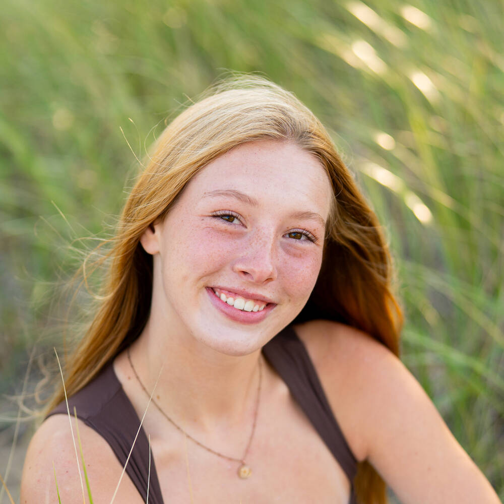 Young woman with strawberry blonde hair smiling against a background of beach grass